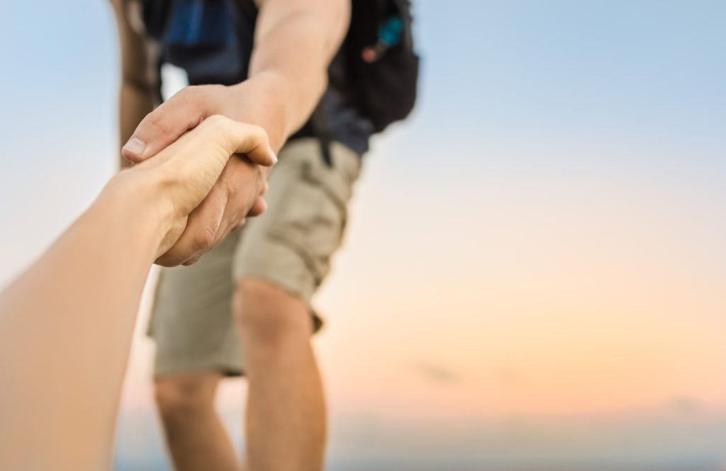 Close-up of a hiker reaching down to pull another person up by the hand.