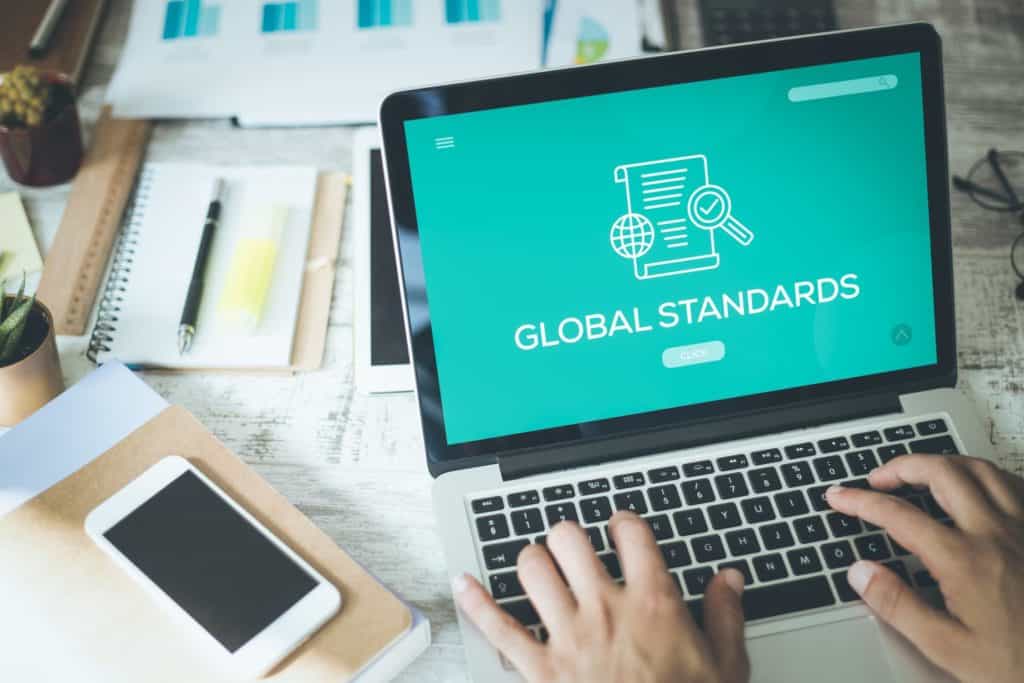 Person typing on a laptop displaying "Global Standards" on the screen.